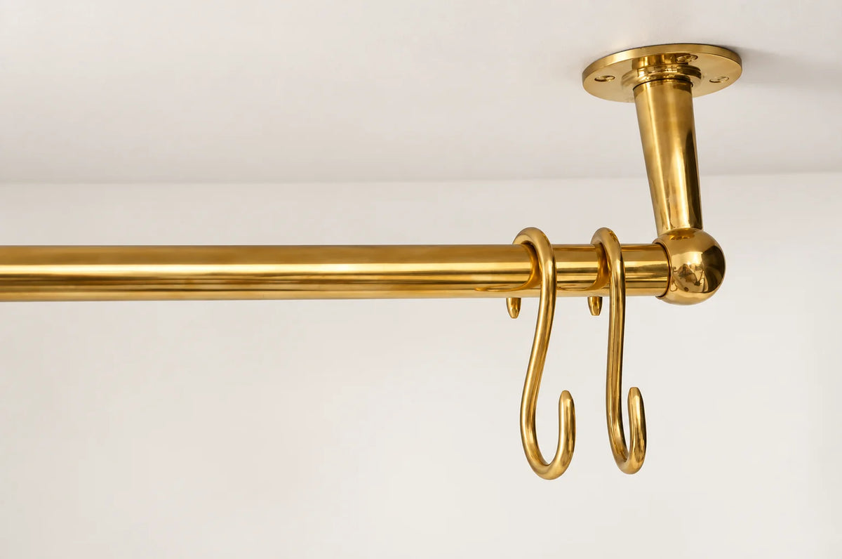 A polished brass hanging rod with two hooks, mounted to a ceiling with a matching ceiling mount, shown against a plain white wall.