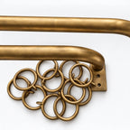 Close-up of a brass wall-mounted towel bar with a decorative cluster of interlocking rings on the left side, shown against a plain white background.