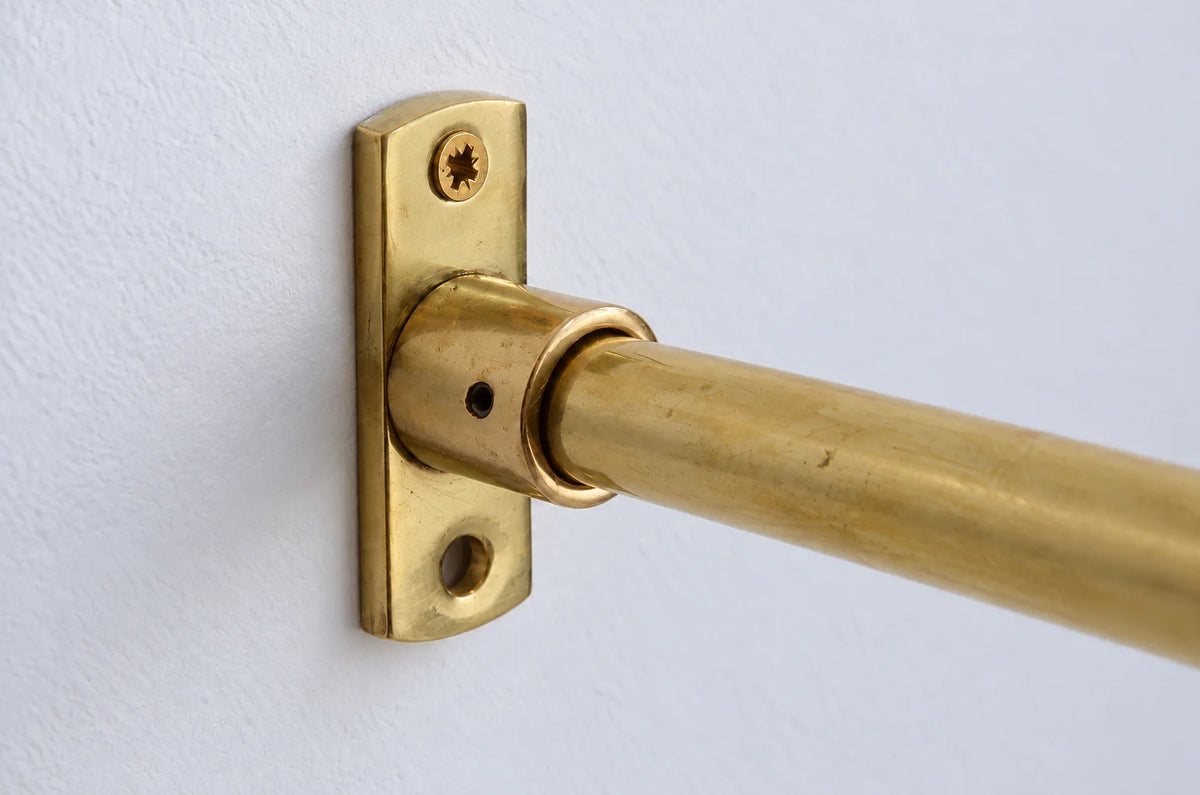 A close-up of a brass curtain rod mounted on a white wall with a matching brass wall plate.