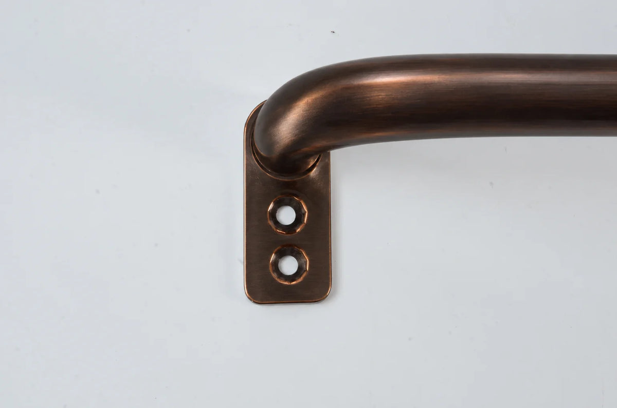 A close-up of a curved metal bar with a square mounting plate featuring two screw holes, finished in a warm bronze/copper tone against a plain light background.