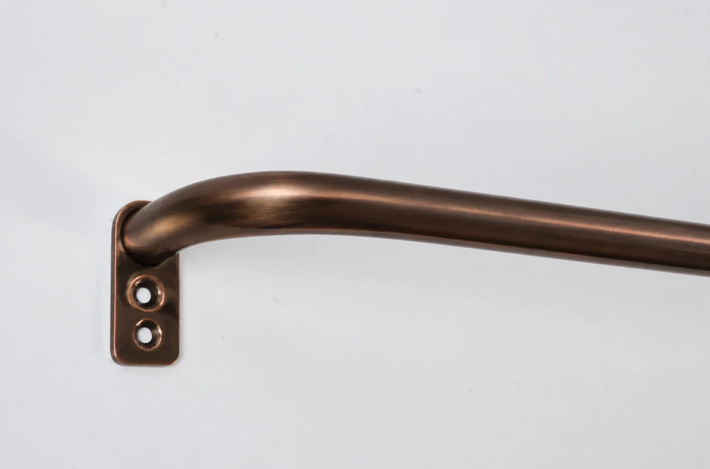 A close-up of a curved brass rod with a matching wall bracket, finished in a warm bronze color, set against a plain light gray background.