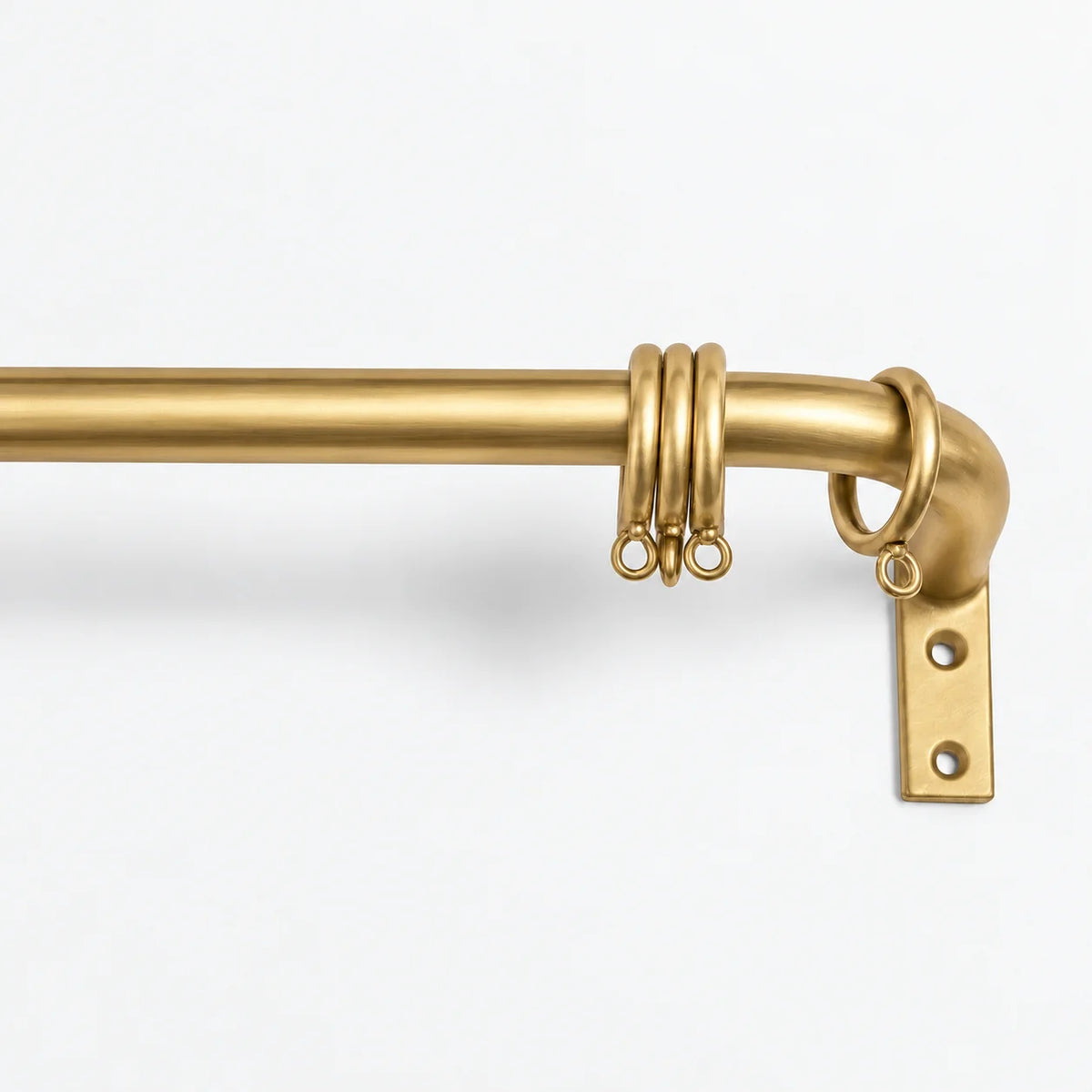 A close-up of a brass curtain rod with a corner bracket and decorative hanging rings, shown against a plain white background.