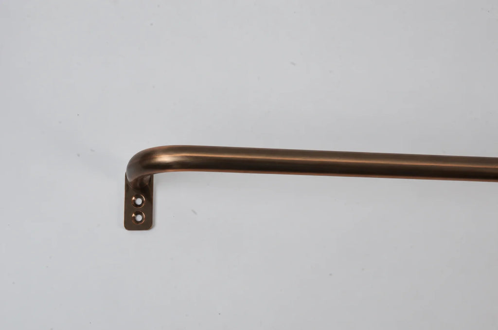 A close-up of a curved metal bar with a square mounting bracket, finished in a warm bronze or copper tone, shown against a plain light gray background.